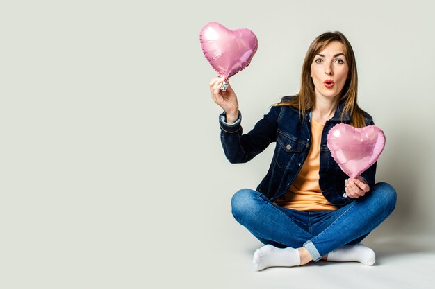 Vriendelijke jonge vrouw zitten met gekruiste benen met luchtballonnen in de vorm van een hart