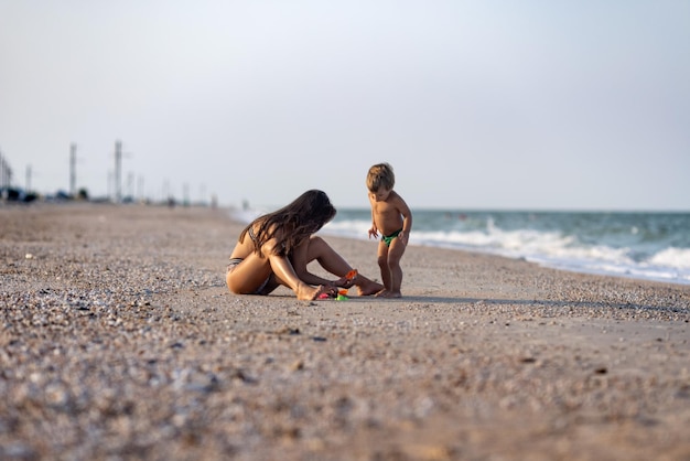 Vriendelijke magere schattige oudere zus speelt met haar kleine broertje peuter zittend op het ondiepe zeewater in de buurt van de kust op een warme zonnige dag op zomervakantie