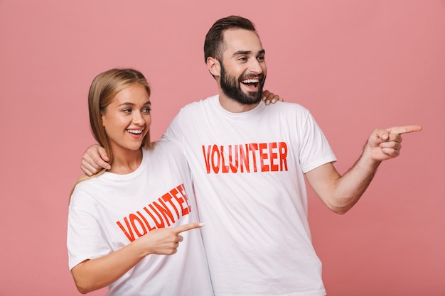 vriendelijke man en vrouw vrijwilligers dragen uniforme t-shirts wijzende vingers opzij geïsoleerd