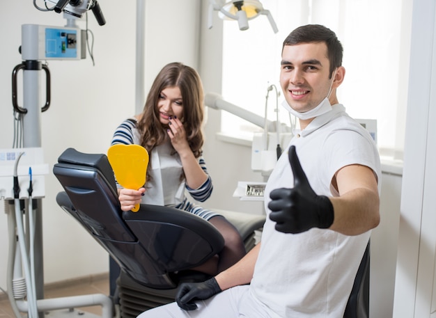 Vriendelijke mannelijke tandarts met aantrekkelijke vrouwelijke patiënt na behandeling in moderne tandheelkundige kliniek.