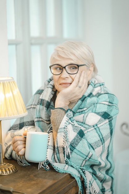 Vriendelijke oude oma die aan iets denkt en thee drinkt