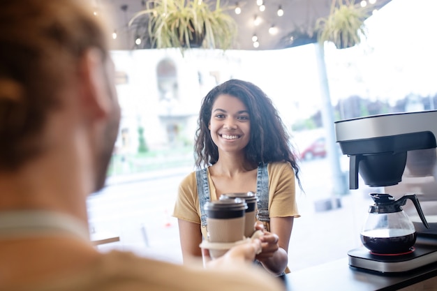 Foto vriendelijke service. gelukkige mooie jonge vrouw die bestelde afhaalkoffie neemt die zich voor barista in koffie bevindt