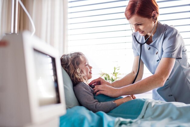 Vriendelijke vrouwelijke dokter onderzoekt een klein meisje in bed in het ziekenhuis