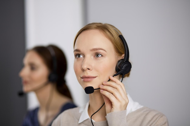 Vriendelijke zakenvrouw die via de headset praat terwijl ze op kantoor zit. Callcenter en diverse groep mensen in het bedrijfsleven.