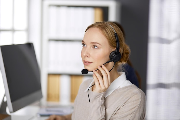 Vriendelijke zakenvrouw die via de headset praat terwijl ze op kantoor zit. Callcenter en diverse mensengroep in het bedrijfsleven