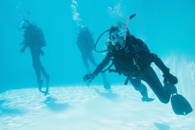 Vrienden bij scuba-training trainen ondergedompeld in zwembad één op zoek naar camera