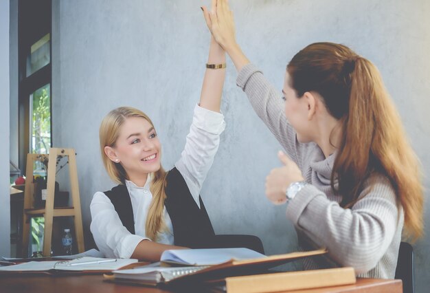 Foto vrienden die high-five doen terwijl ze aan het bureau tegen de muur zitten.