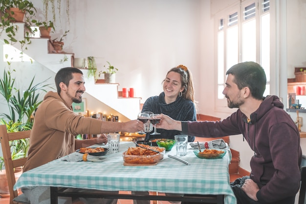 Vrienden die plezier hebben tijdens het diner aan de eettafel thuis Vrolijk eten, roosteren en genieten