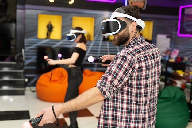 Vrienden, een man en een vrouw gebruiken een virtual reality-headset met bril en handbewegingscontrollers in de speelruimte. Moderne technologieën concept afbeelding.