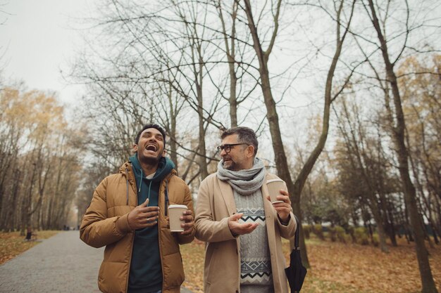 Vrienden een senior en een jonge man die samen loopt en praat en koffie drinkt in het herfstparkxA