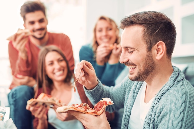 Vrienden en pizza. Vier jonge vrolijke mensen die pizza thuis eten.