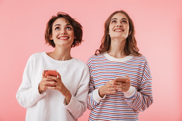 Vrienden geïsoleerd over roze muur met behulp van mobiele telefoons.