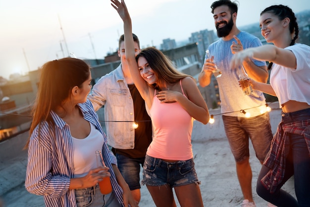 Vrienden genieten van cocktails op een feestje. Groep gelukkige mensen die plezier hebben, dansen op een dak