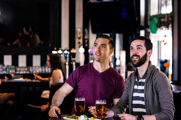 Vrienden hebben een pint en kijken tv in een bar