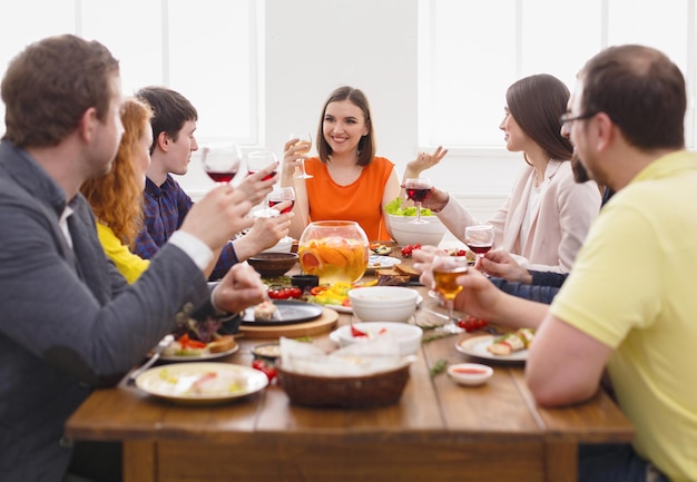 Vrienden hebben feestdiner in café, restaurant. Jong bedrijf viert met alcohol en eten aan houten tafel binnenshuis.