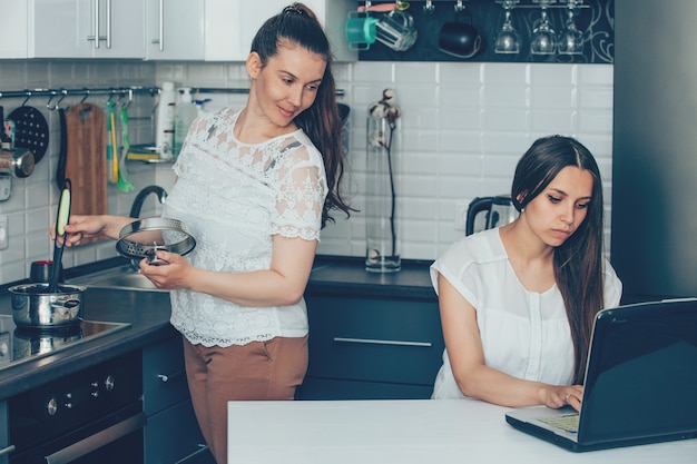 Vrienden in de keuken die aan laptop werken en koken