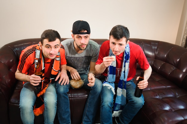 Vrienden juichen en drinken van alcohol tijdens het kijken naar voetbalwedstrijd op tv.