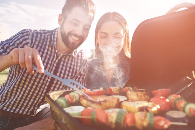 Vrienden maken barbecue en lunchen in de natuur. paar plezier tijdens het eten en drinken op een picknick - gelukkige mensen op bbq party.