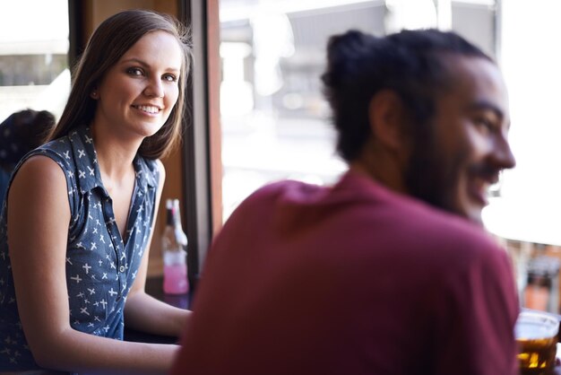 Vrienden man en vrouw in de pub met bier drinken en ontspannen in sociaal evenement of feest met gesprek venster uitzicht mensen en alcohol in de club met glas of glimlach binding en viering in het restaurant