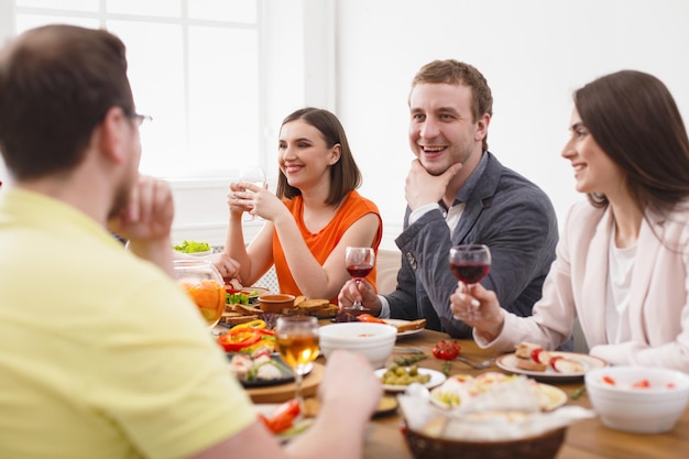 Vrienden ontmoeten. groep gelukkige mensen die praten, eten, gezonde maaltijden doorgeven aan de feesttafel in café, restaurant. jong bedrijf viert met alcohol en eten aan houten tafel binnenshuis.