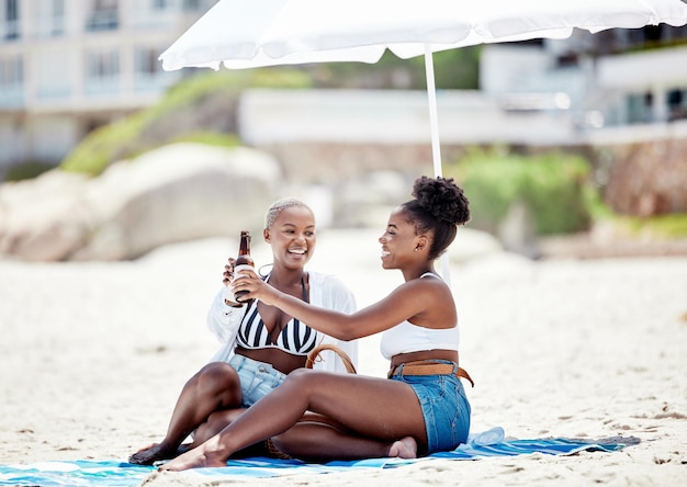 Vrienden ontspannen en een biertje drinken op het strand terwijl ze samen op vakantie zijn in de zomer Gelukkige zwarte vrouwen die een toast maken met alcohol terwijl ze aan de oceaan zitten terwijl ze op vakantie zijn in Zuid-Afrika