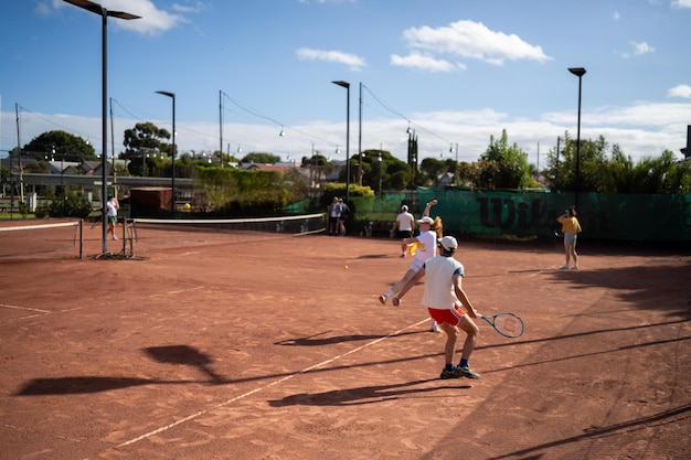 Vrienden spelen tennis op een kleibaan, water geven en een kleienbaan in zakken stoppen, tennisbaan onderhouden.