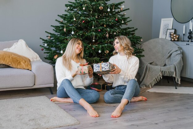 Vrienden van de zusterschap in gezellige kleren glimlachen wijd en wisselen kerstcadeaus uit in een feestelijke doos onder de kerstboom