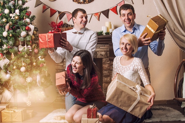 Vrienden van vier mannen en vrouwen geven cadeautjes onder de boom in het kerstinterieur