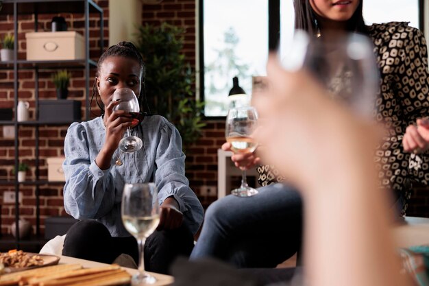 Vrienden verzamelden zich met een wijnfeest thuis in de woonkamer terwijl ze een verjaardagsevenement vierden. Gelukkige groep jonge volwassen mensen die samen ontspannen terwijl ze genieten van het drinken van wijn en binding.