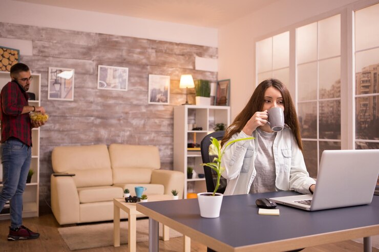 Foto vriendin neemt een slokje koffie terwijl ze aan een laptop werkt in de woonkamer. vriendje aan de telefoon en op de achtergrond chips aan het eten.