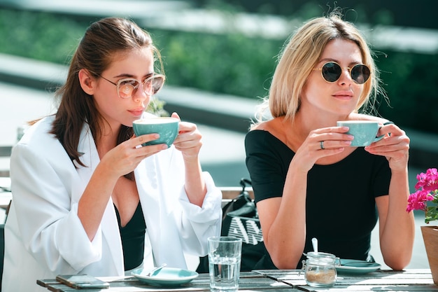 Vriendinnen in café buiten twee mooie meisjes met kopjes koffie in zomercafé buiten portret o