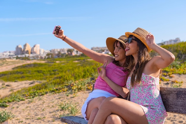 Vriendinnen in hoed erg blij op strandvakantie een selfie maken met telefoon zomer reizen vrienden vriendschap concept