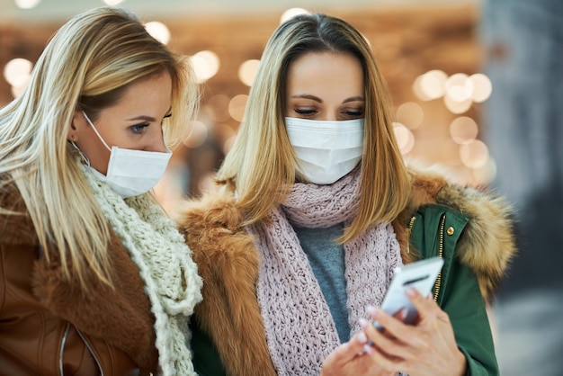 Vriendinnen met smartphone winkelen samen met het masker coronavirus concept