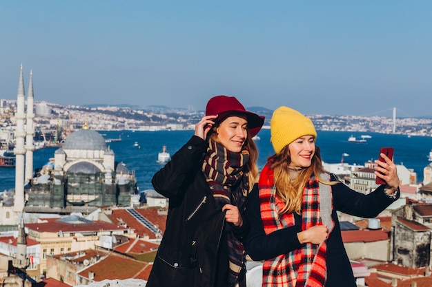 Vriendinnen nemen een selfie op het dak van de grand bazaar, istanbul, turkije. twee glimlachende meisjes zijn gefotografeerd aan de telefoon tegen de achtergrond van istanbul op een heldere winterdag.