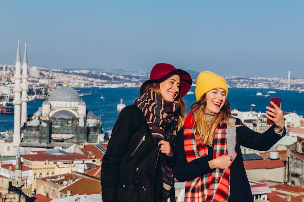 Vriendinnen nemen een selfie op het dak van de Grand Bazaar, Istanbul, Turkije. Twee glimlachende meisjes zijn gefotografeerd aan de telefoon tegen de achtergrond van Istanbul op een heldere winterdag.