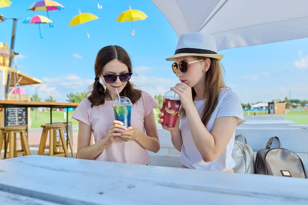 Vriendinnen tieners die plezier hebben met het drinken van frisdrank terwijl ze op een zonnige zomerdag op een terras zitten, vriendschap adolescentie vakantie concept