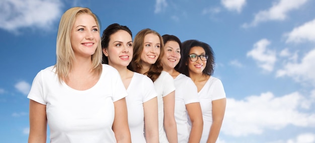 Foto vriendschap, divers, lichaamspositief en mensenconcept - groep gelukkige vrouwen van verschillende grootte in witte t-shirts over blauwe lucht en wolkenachtergrond