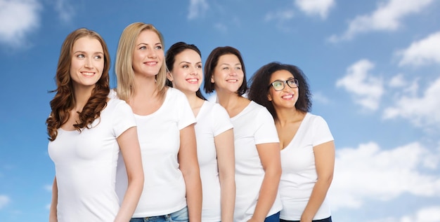 Foto vriendschap, divers, lichaamspositief en mensenconcept - groep gelukkige vrouwen van verschillende grootte in witte t-shirts over blauwe lucht en wolkenachtergrond