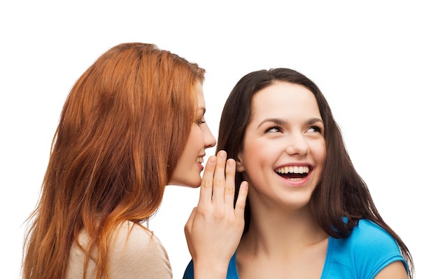 vriendschap, geluk en mensenconcept - twee glimlachende meisjes die roddels fluisteren
