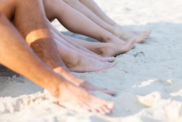 vriendschap, geluk, zomervakantie, vakantie en mensenconcept - close-up van vrienden die op het strand zitten