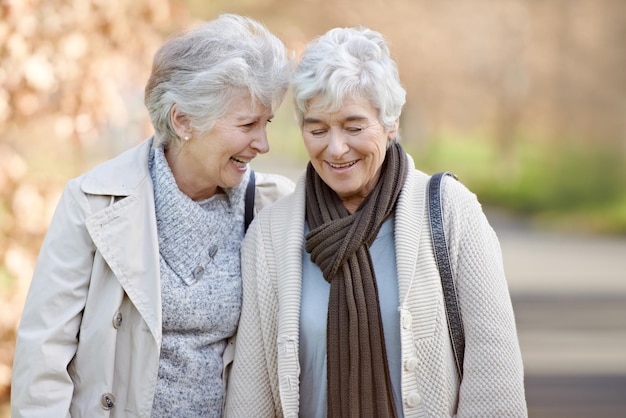 Vriendschap in hun herfstjaren twee oudere vrouwen hebben een vriendelijk gesprek buiten met herfstbladeren op de achtergrond