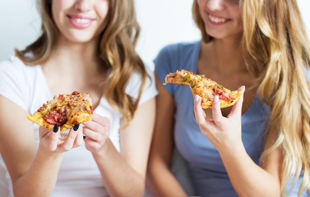 Foto vriendschap, mensen, pyjamafeest en junkfood concept - close-up van gelukkige vrienden of tienermeisjes die thuis pizza eten