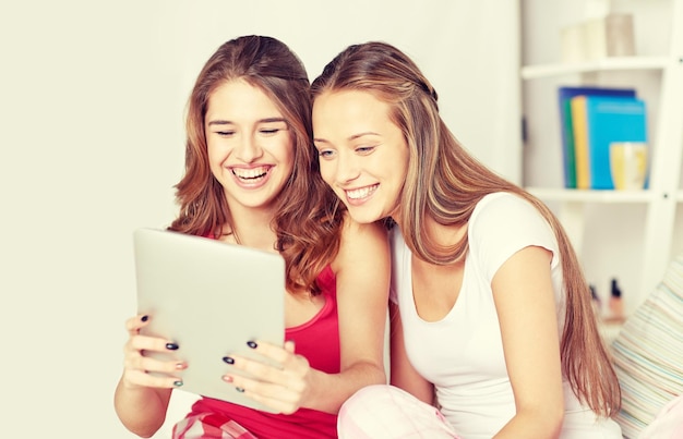 vriendschap, mensen, pyjamafeest en technologieconcept - gelukkige vrienden of tienermeisjes met tablet pc-computer thuis