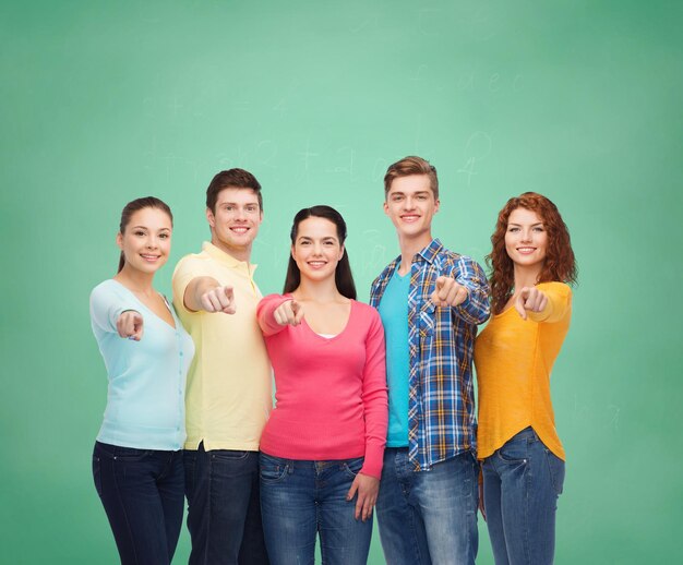 vriendschap, onderwijs, school en mensenconcept - groep glimlachende tieners die vinger op u richten over groene raadsachtergrond