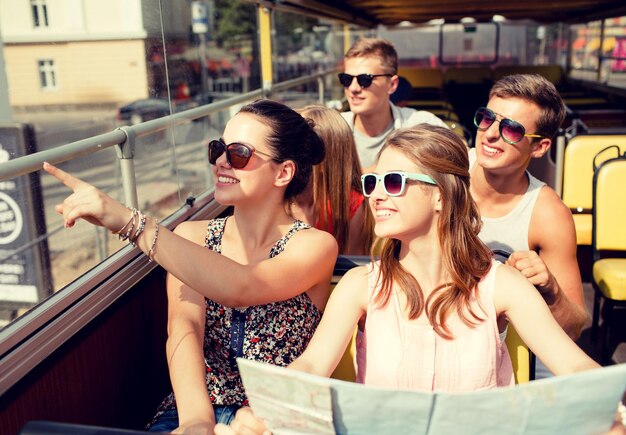 vriendschap, reizen, vakantie, zomer en mensen concept - groep lachende vrienden met kaart reizen met de tourbus
