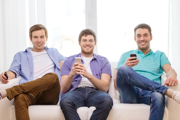 vriendschap, technologie en thuisconcept - lachende mannelijke vrienden met smartphones thuis
