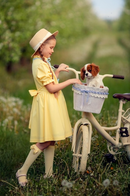 Vriendschap van kinderen en huisdieren een schattig meisje en een kleine cavalier van een puppy fietsen in het voorjaar in een bloeiende tuin