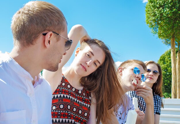 Vriendschap, vrije tijd, snoep, zomer en mensen concept - groep lachende vrienden met ijs buitenshuis. Studenten in het park op een zonnige zomerdag, zittend op een bankje, ijs etend