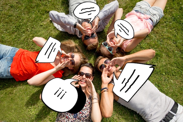 vriendschap, vrije tijd, zomer, bericht en mensenconcept - groep glimlachende vrienden die met tekstbelkrabbels in cirkel op gras buitenshuis liggen