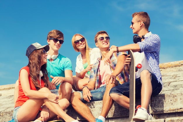 vriendschap, vrije tijd, zomer en mensen concept - groep lachende vrienden met skateboard zittend op straat in de stad